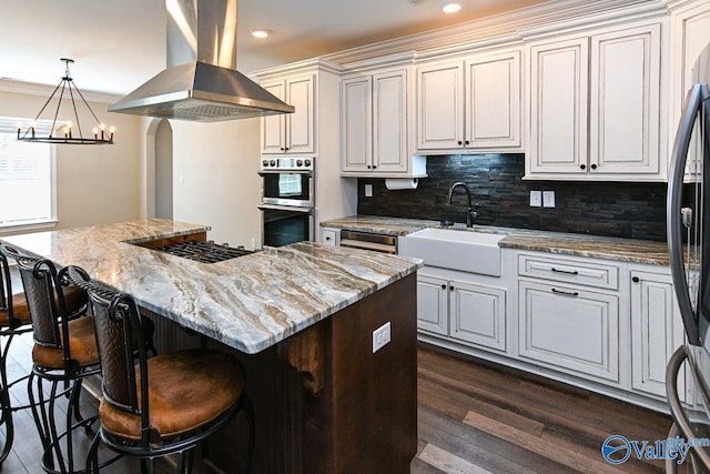 kitchen with a sink, a kitchen island, island exhaust hood, and light stone countertops