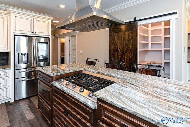 kitchen with light stone countertops, a barn door, island exhaust hood, and stainless steel appliances