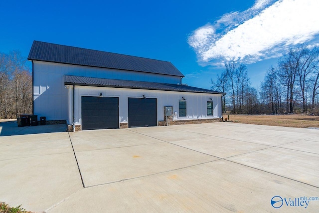 exterior space featuring metal roof, an attached garage, stone siding, concrete driveway, and board and batten siding