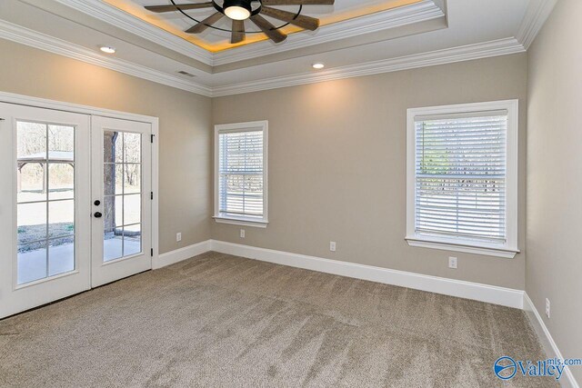 carpeted spare room with a tray ceiling, french doors, visible vents, ornamental molding, and baseboards