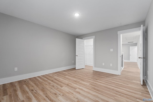 unfurnished bedroom with a walk in closet, a closet, and light wood-type flooring