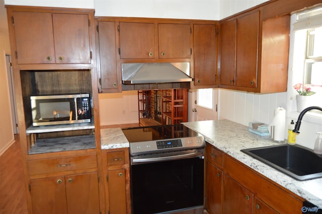 kitchen featuring stainless steel appliances, light stone countertops, wall chimney range hood, and sink