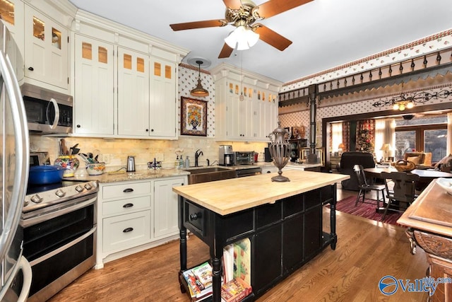 kitchen featuring sink, hardwood / wood-style flooring, appliances with stainless steel finishes, white cabinets, and decorative light fixtures