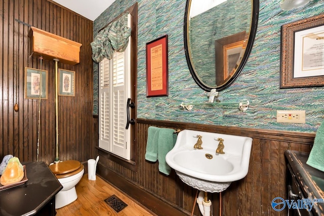bathroom featuring wooden walls, wood-type flooring, toilet, and sink