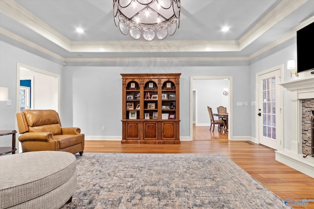 living room with a chandelier, light hardwood / wood-style floors, a tray ceiling, and crown molding