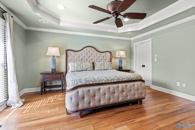 bedroom featuring wood-type flooring, a tray ceiling, ceiling fan, and ornamental molding