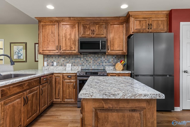 kitchen with a sink, brown cabinetry, wood finished floors, stainless steel appliances, and backsplash