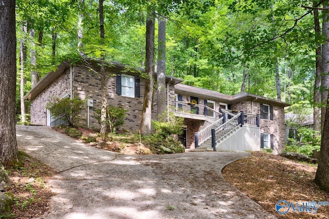view of front of property with driveway, brick siding, a view of trees, stairs, and a deck