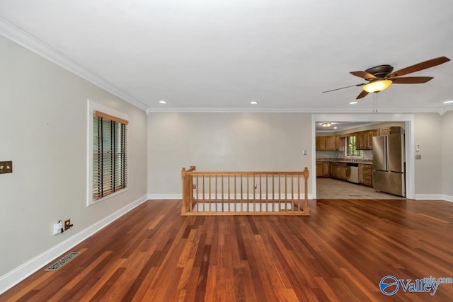 spare room with baseboards, ornamental molding, ceiling fan, visible vents, and wood finished floors