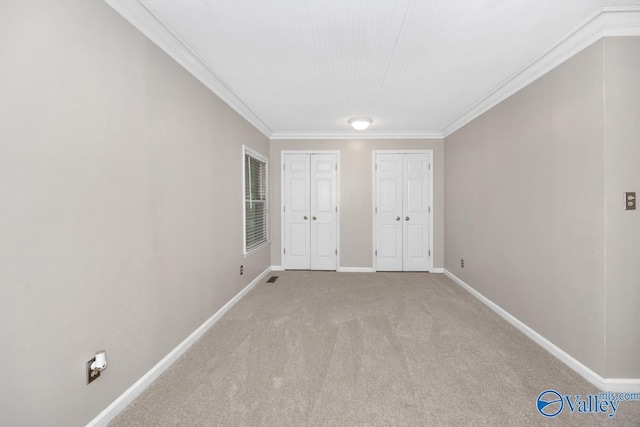 unfurnished bedroom with baseboards, carpet flooring, visible vents, crown molding, and multiple closets