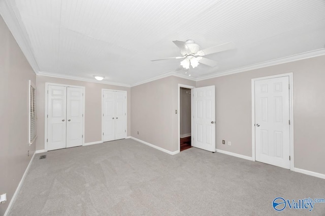 unfurnished bedroom featuring carpet flooring, crown molding, baseboards, and multiple closets