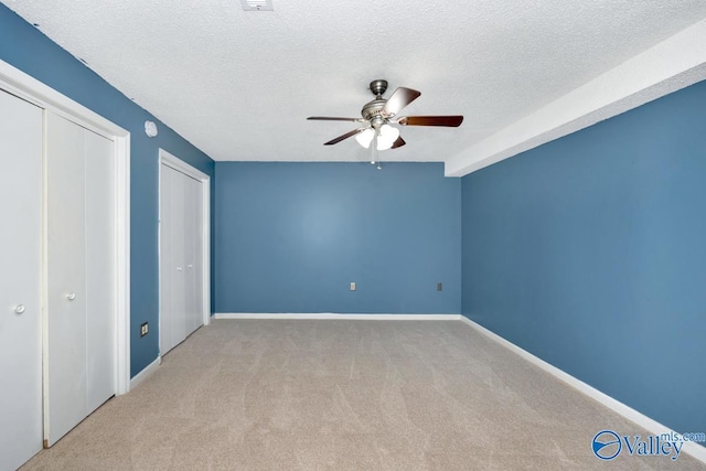 unfurnished bedroom featuring a textured ceiling, baseboards, two closets, and carpet