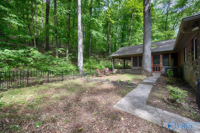view of yard with fence, a view of trees, and central AC