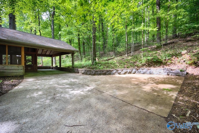 view of patio featuring concrete driveway, a carport, and a view of trees