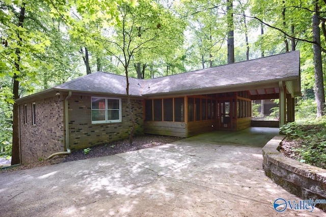 single story home with an attached carport, a sunroom, concrete driveway, brick siding, and roof with shingles