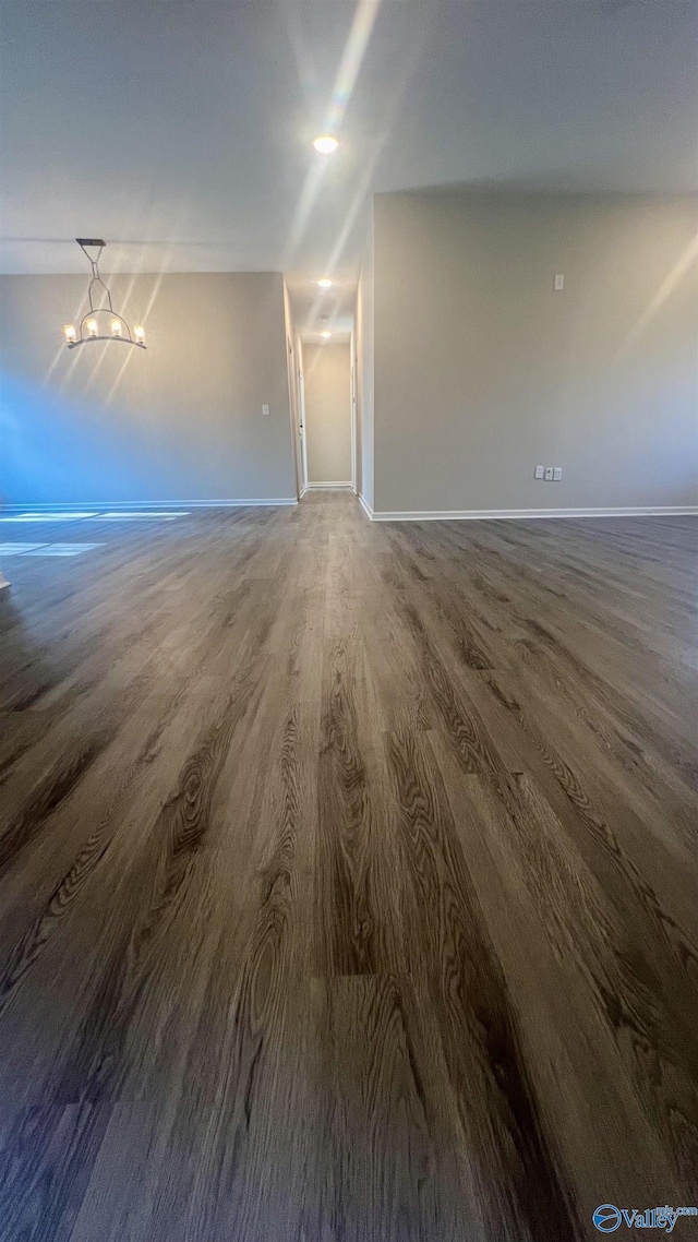 unfurnished living room with a notable chandelier, baseboards, and wood finished floors