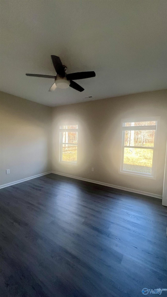 empty room with dark wood-type flooring, visible vents, ceiling fan, and baseboards