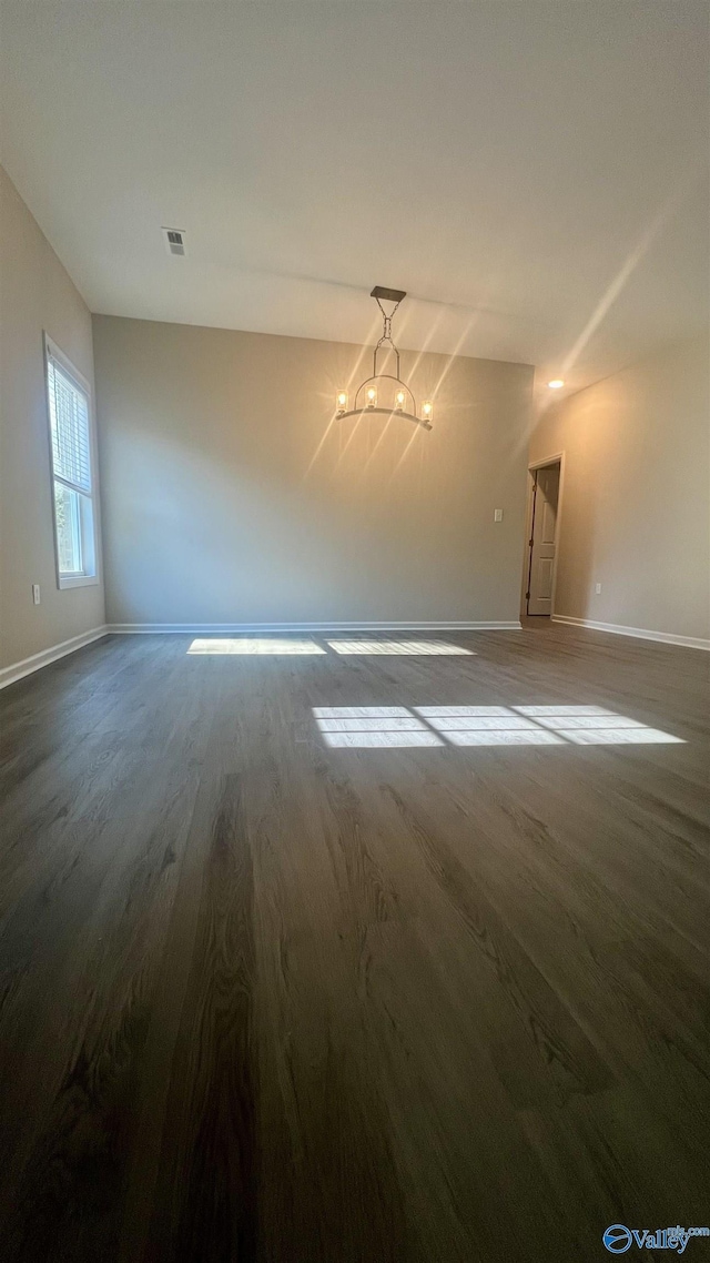 empty room featuring a chandelier, dark wood finished floors, visible vents, and baseboards