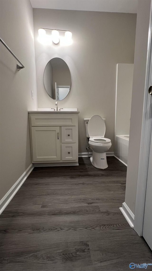 full bath featuring toilet, wood finished floors, vanity, baseboards, and a bath