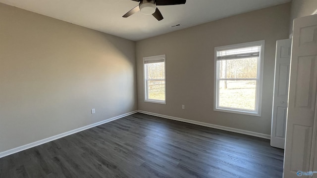 empty room featuring a wealth of natural light, dark wood-style flooring, and baseboards