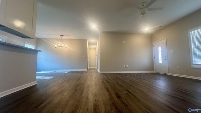 unfurnished living room with baseboards, dark wood-type flooring, and ceiling fan with notable chandelier