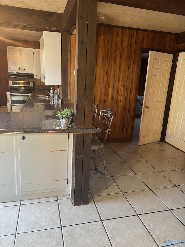 kitchen featuring electric stove, light tile patterned floors, white cabinets, a sink, and wooden walls