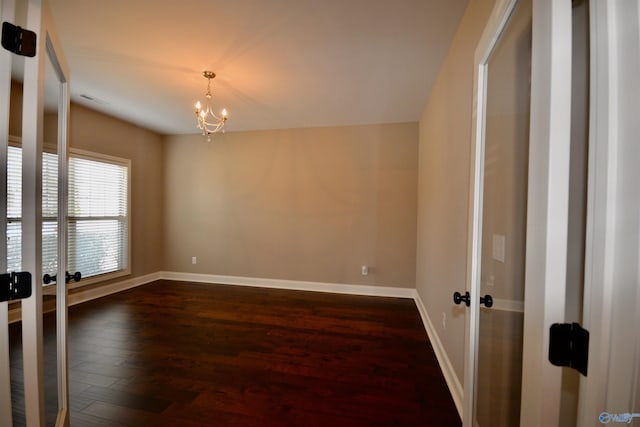 unfurnished room featuring dark wood-type flooring, a notable chandelier, visible vents, and baseboards