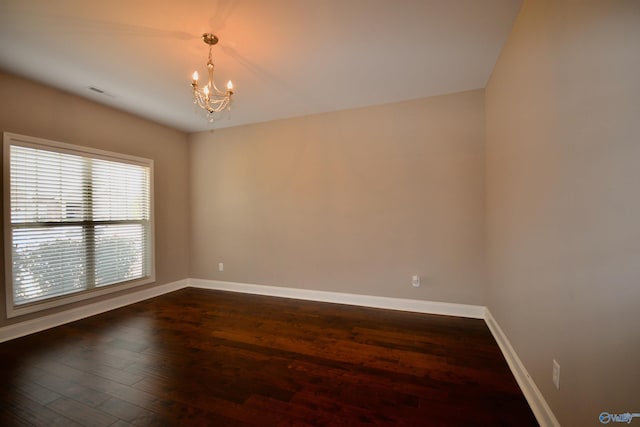 unfurnished room with an inviting chandelier, dark wood-type flooring, visible vents, and baseboards