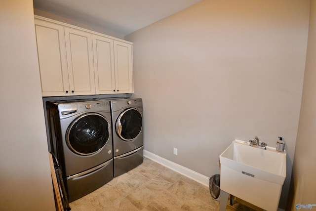 clothes washing area featuring a sink, baseboards, cabinet space, and separate washer and dryer