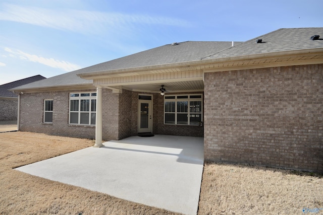 rear view of property with a patio area, a ceiling fan, brick siding, and a shingled roof