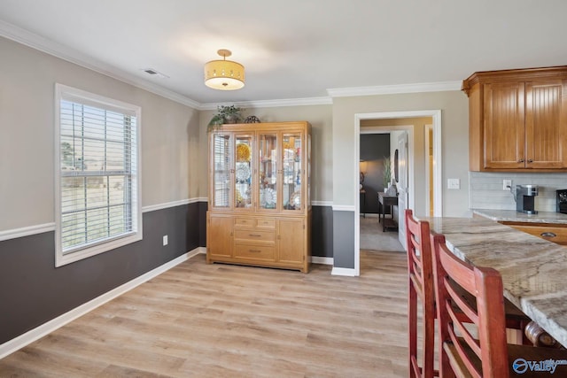 dining space featuring light wood-type flooring, baseboards, visible vents, and ornamental molding