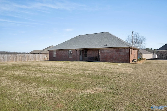 rear view of house featuring a yard, brick siding, a shingled roof, and fence