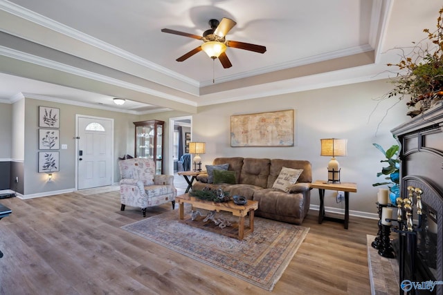living room with light wood finished floors, baseboards, a raised ceiling, and crown molding