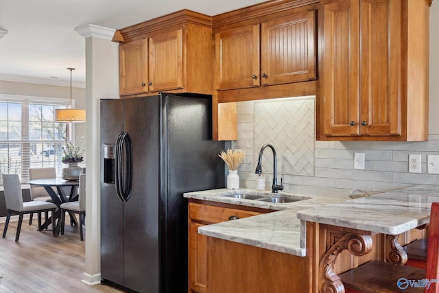 kitchen featuring light stone counters, a sink, ornamental molding, black fridge, and brown cabinets