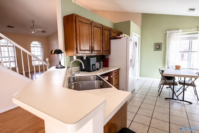 kitchen featuring visible vents, brown cabinetry, vaulted ceiling, a sink, and a peninsula