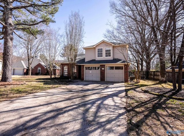 view of front of property with driveway, brick siding, an attached garage, and fence