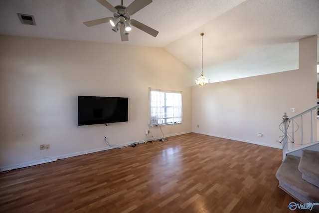 unfurnished living room featuring stairs, visible vents, vaulted ceiling, wood finished floors, and ceiling fan with notable chandelier