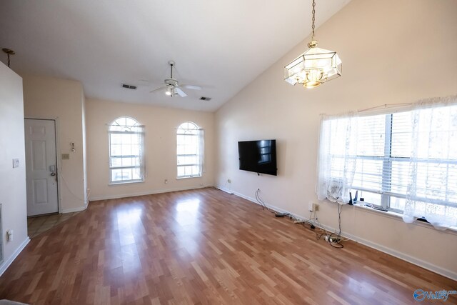 unfurnished living room featuring ceiling fan with notable chandelier, wood finished floors, visible vents, and lofted ceiling