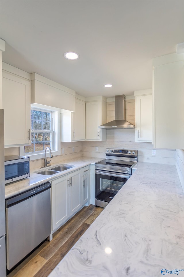 kitchen featuring wall chimney range hood, white cabinets, sink, appliances with stainless steel finishes, and dark wood-type flooring