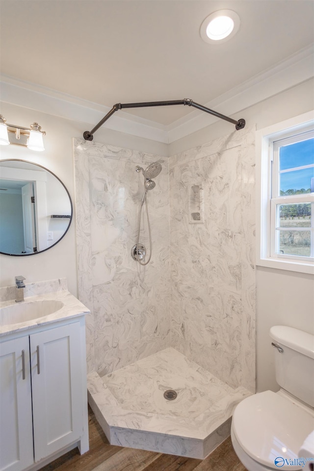 bathroom featuring a tile shower, toilet, vanity, hardwood / wood-style flooring, and ornamental molding