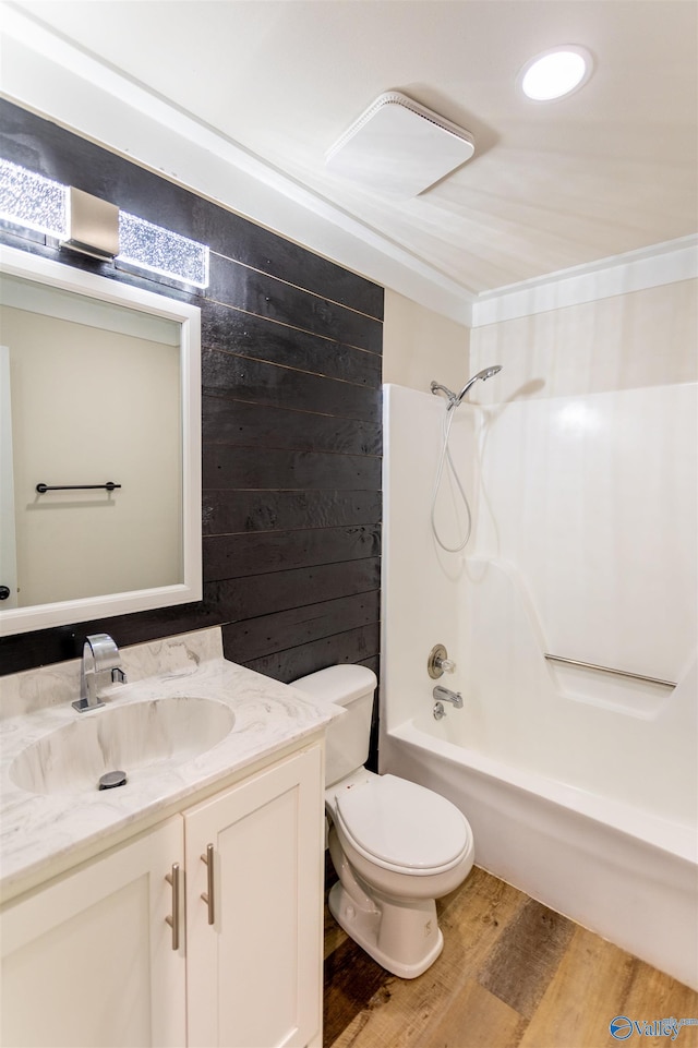 full bathroom featuring vanity, wood-type flooring, wooden walls, shower / washtub combination, and toilet