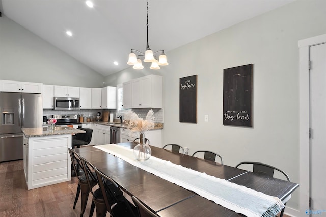 dining area with sink, dark wood-type flooring, high vaulted ceiling, and a chandelier