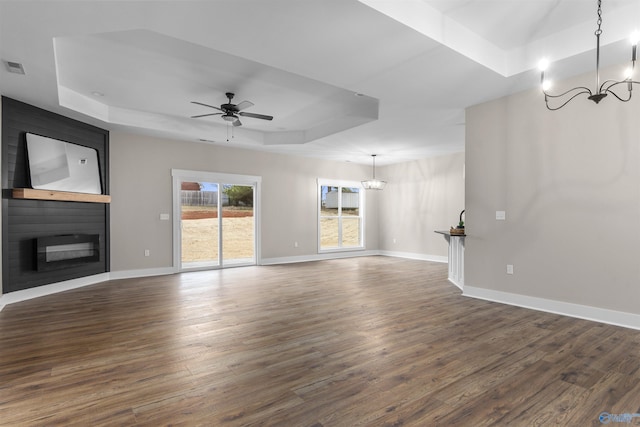 unfurnished living room featuring dark hardwood / wood-style flooring, a tray ceiling, a fireplace, and ceiling fan with notable chandelier