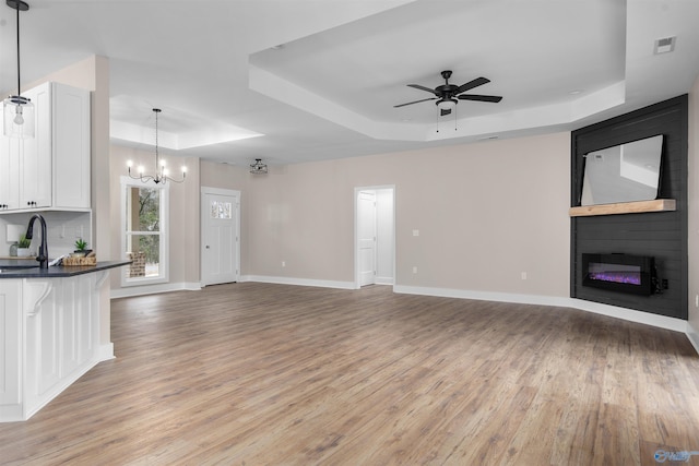 unfurnished living room featuring sink, ceiling fan with notable chandelier, light hardwood / wood-style floors, and a raised ceiling