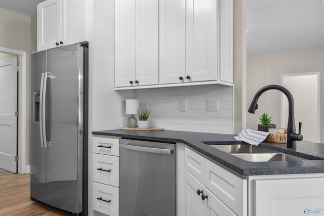 kitchen with sink, white cabinetry, appliances with stainless steel finishes, hardwood / wood-style floors, and backsplash