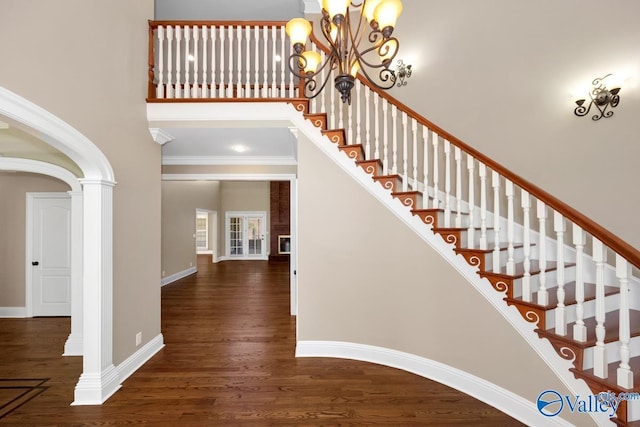 stairs featuring wood finished floors, baseboards, an inviting chandelier, decorative columns, and a towering ceiling