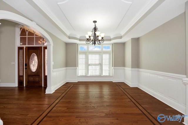 unfurnished dining area featuring a wainscoted wall, arched walkways, a raised ceiling, a chandelier, and dark wood-style flooring