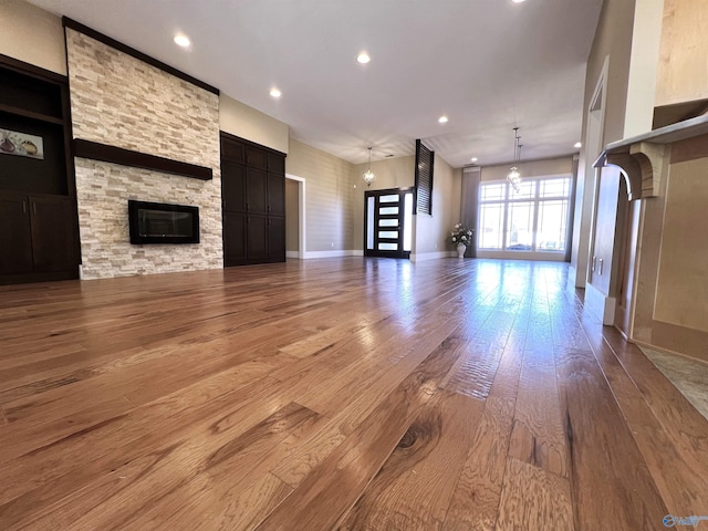 unfurnished living room with baseboards, wood-type flooring, an inviting chandelier, a fireplace, and recessed lighting