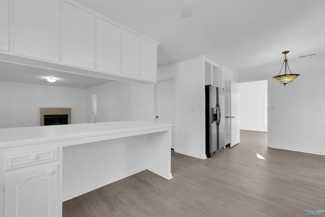 kitchen featuring wood finished floors, baseboards, white cabinets, hanging light fixtures, and stainless steel fridge