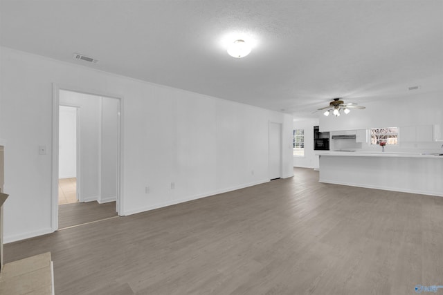 unfurnished living room with a textured ceiling, wood finished floors, visible vents, baseboards, and a ceiling fan